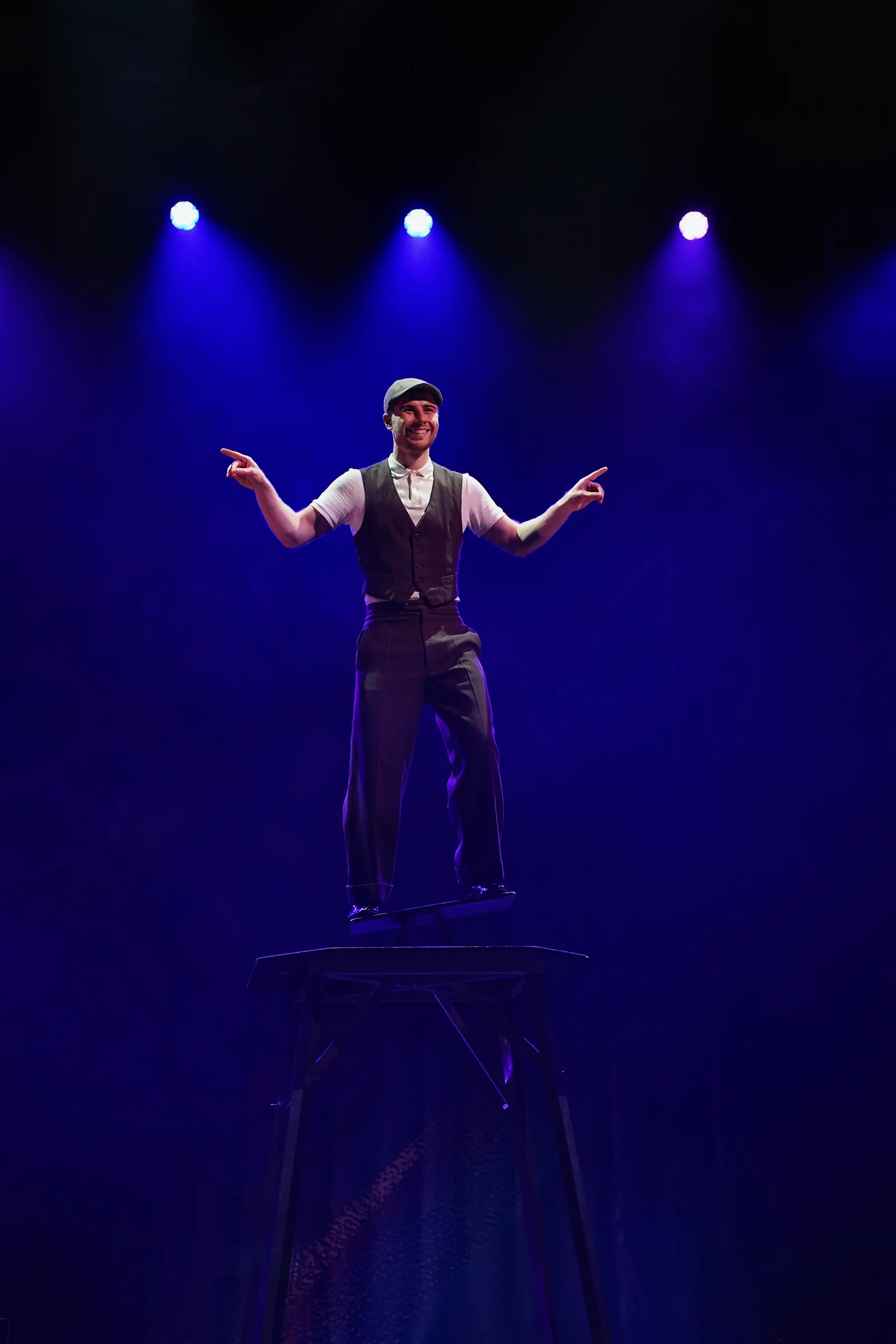 Misha smiling at the audience while balancing on a rola bola board beneath blue stage lights